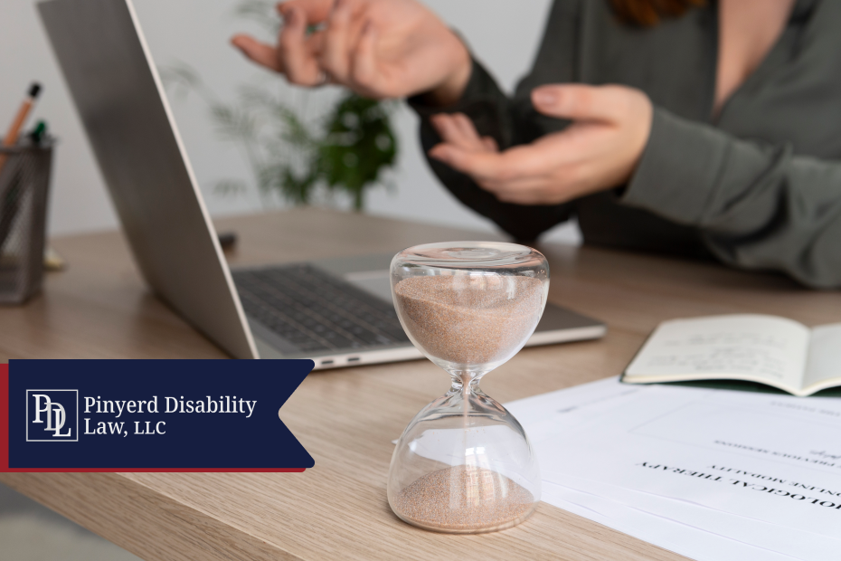 Hourglass on a desk next to a laptop and papers